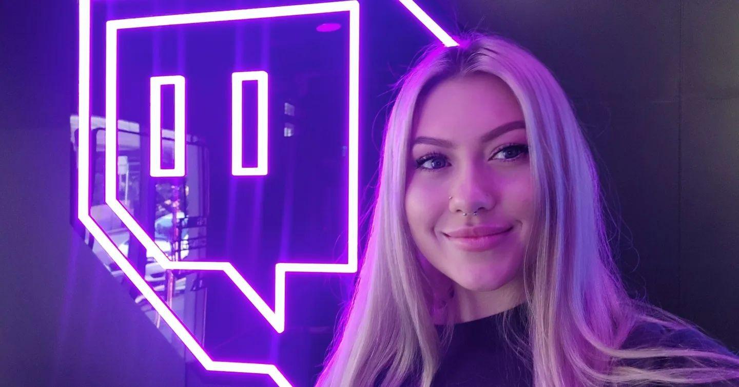 Twitch streamer Primroze smiling in selfie in front of Twitch neon logo